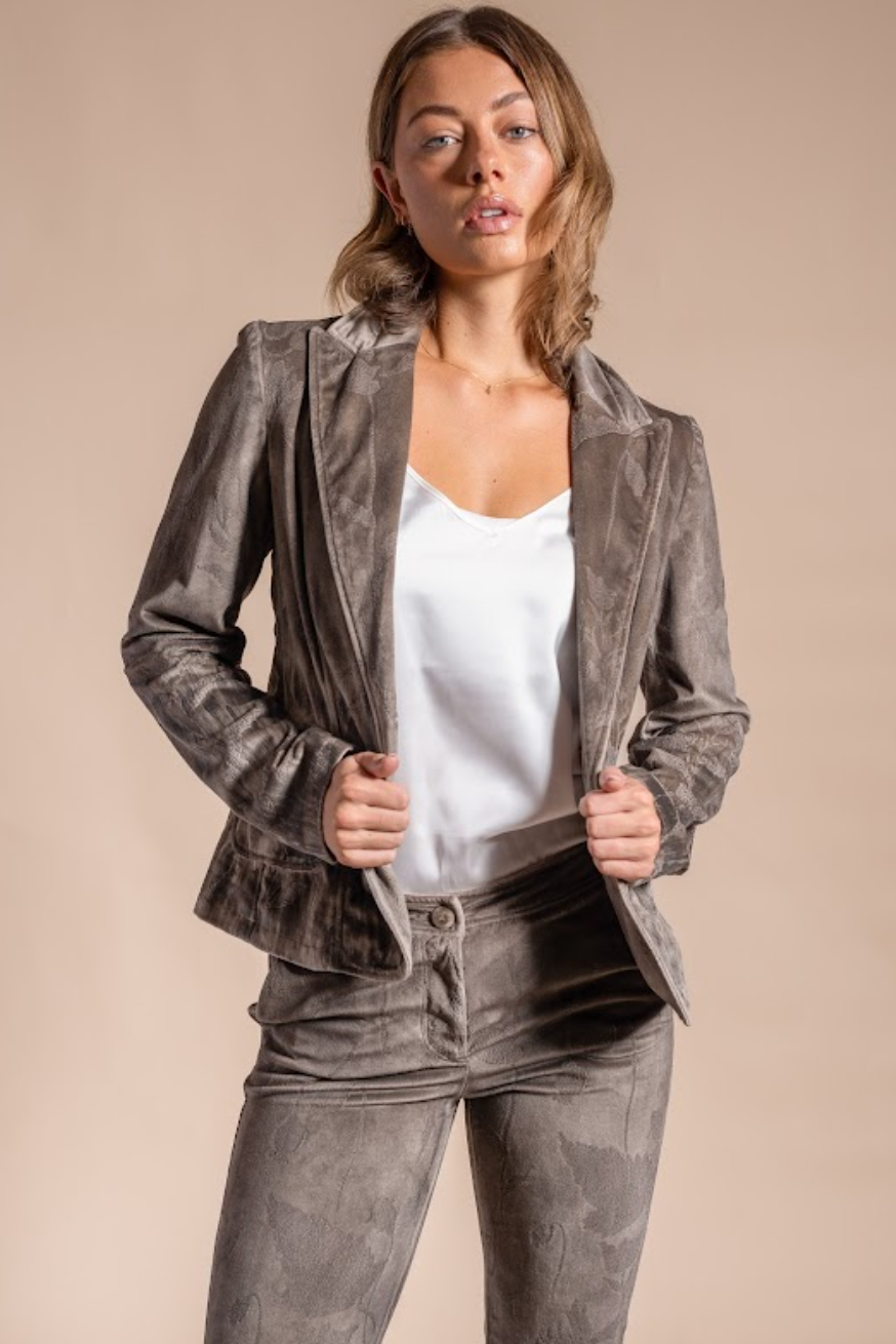 Woman wearing a gray velvet blazer over a white top and gray pants on a beige background