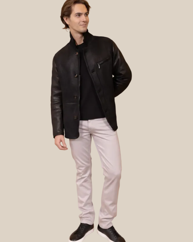 Man wearing a black leather jacket and light gray pants on a brown background