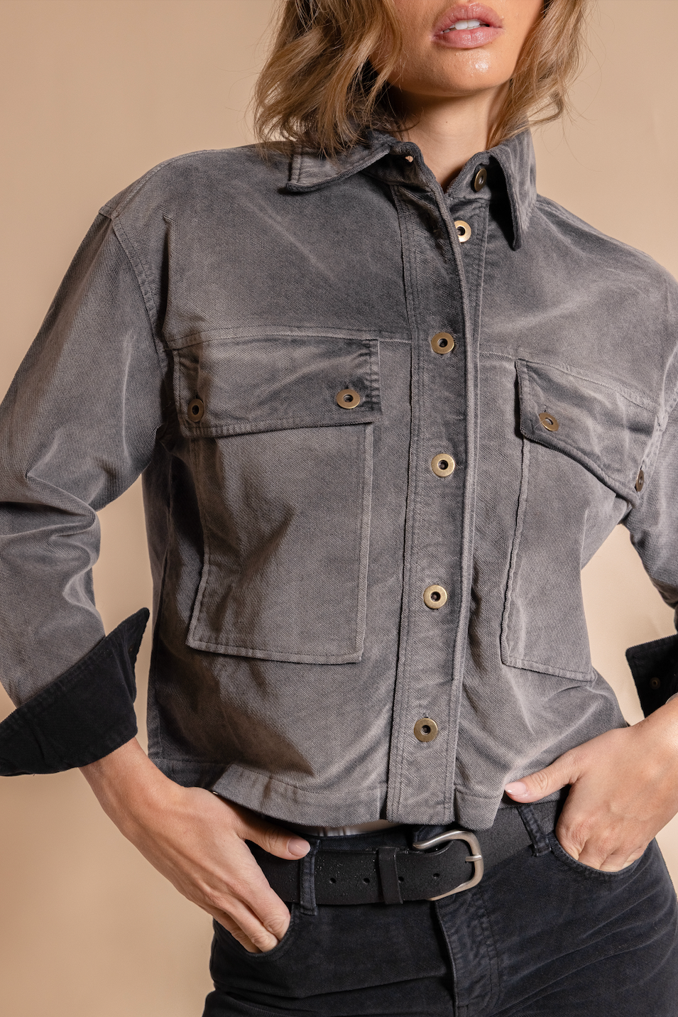 Person wearing a gray button-up shirt with black cuffs on a beige background