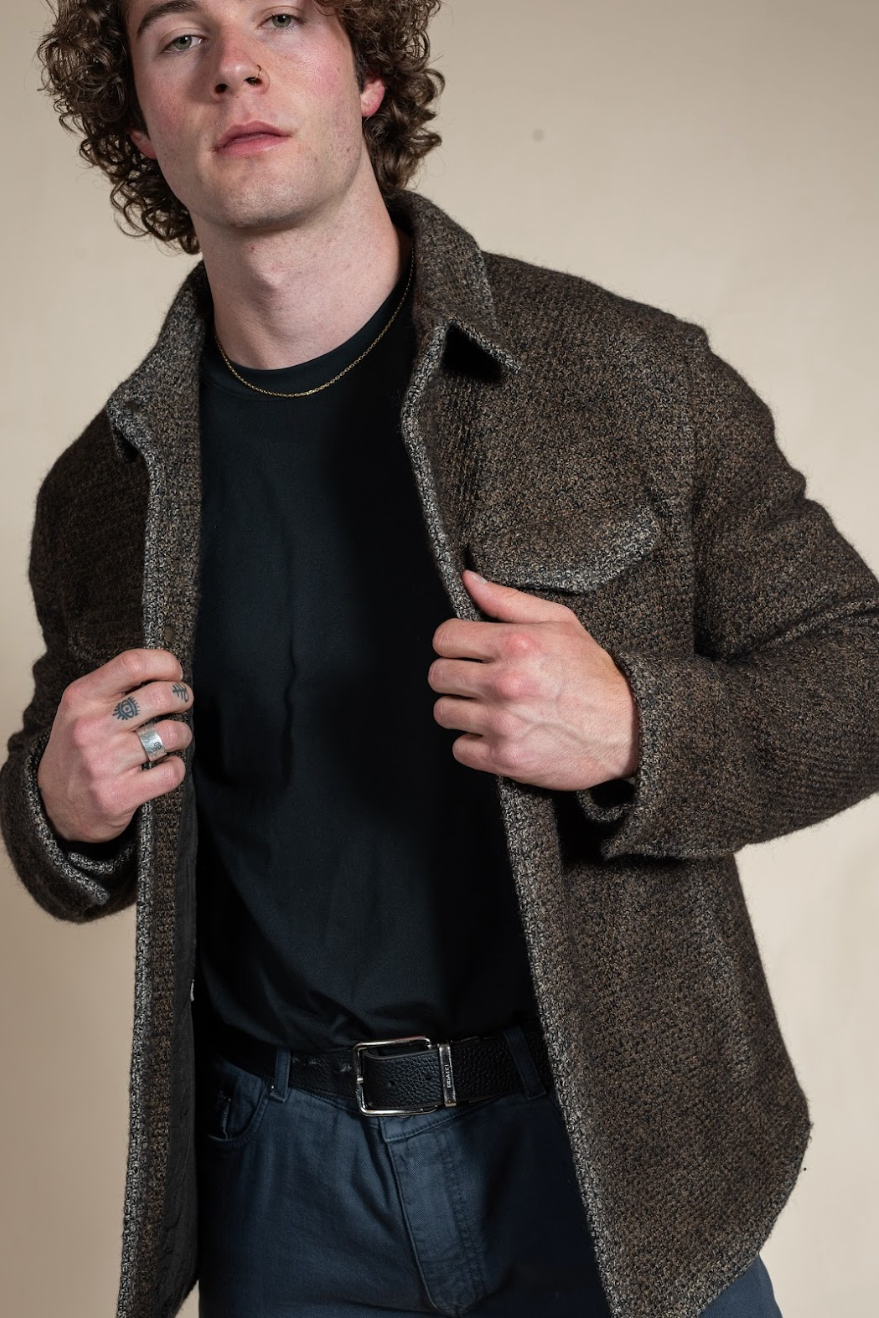 Man wearing a brown coat over a black shirt against a beige background