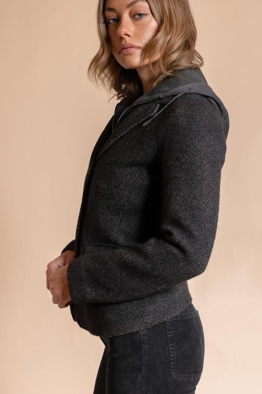 Woman wearing a dark gray hooded jacket against a beige background