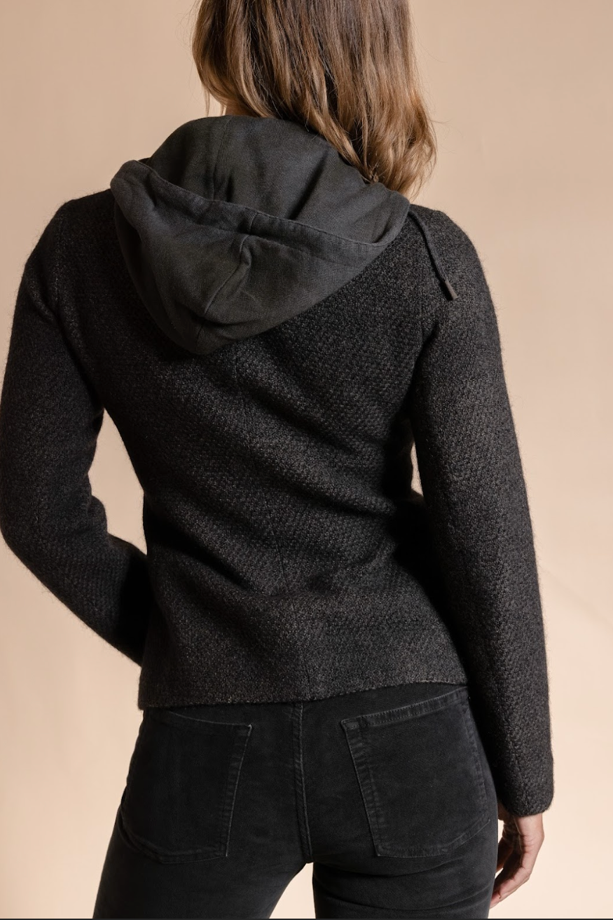 Person wearing a dark gray hooded jacket on a beige background