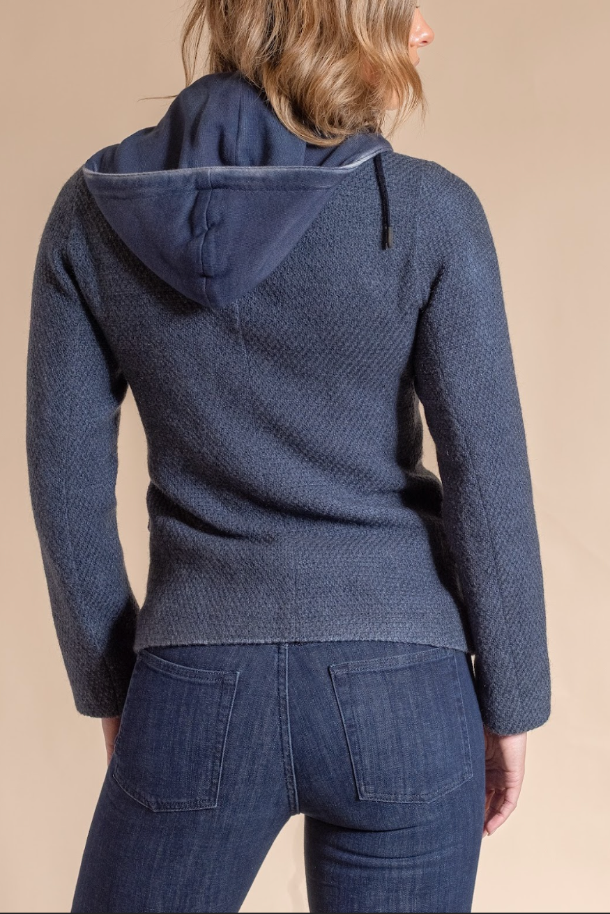 Person wearing a blue hooded jacket and jeans on a beige background