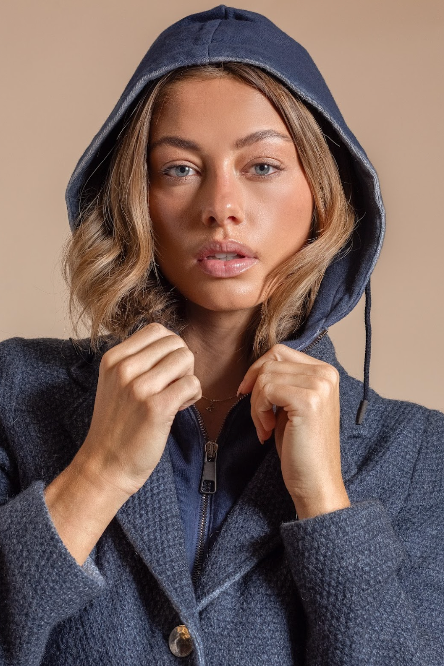 Woman wearing a blue hooded coat against a beige background