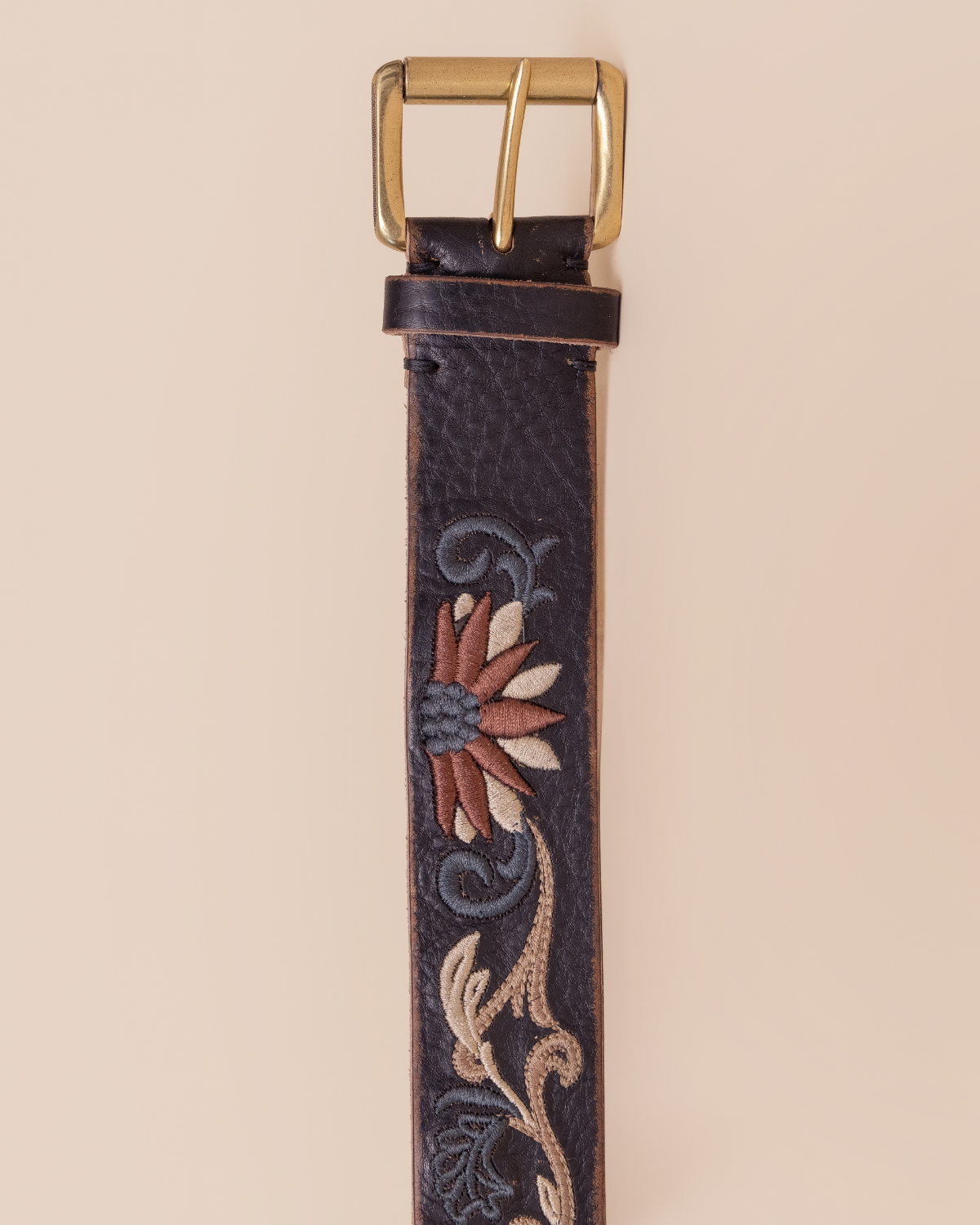 Leather belt with floral embroidery and gold buckle on a beige background