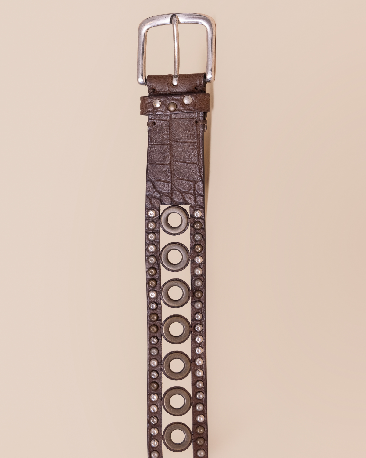 Brown leather belt with circular studs on a beige background