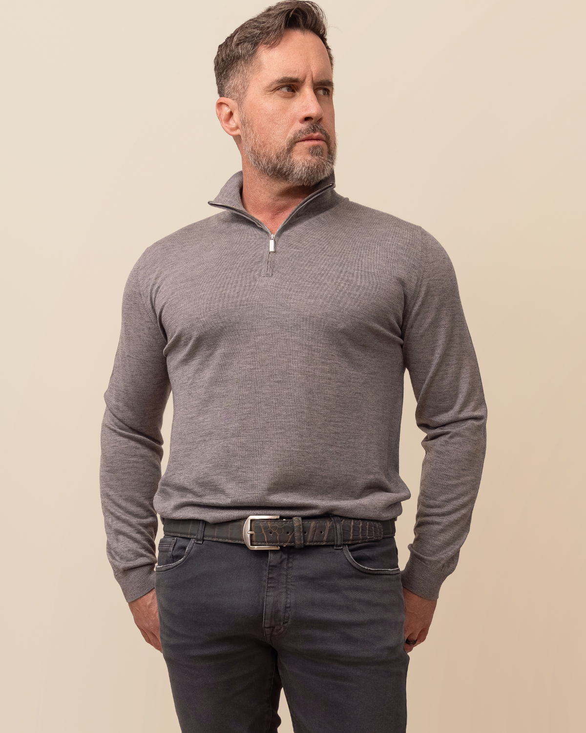 Man wearing a gray long-sleeve shirt with a zipper and dark pants against a beige background