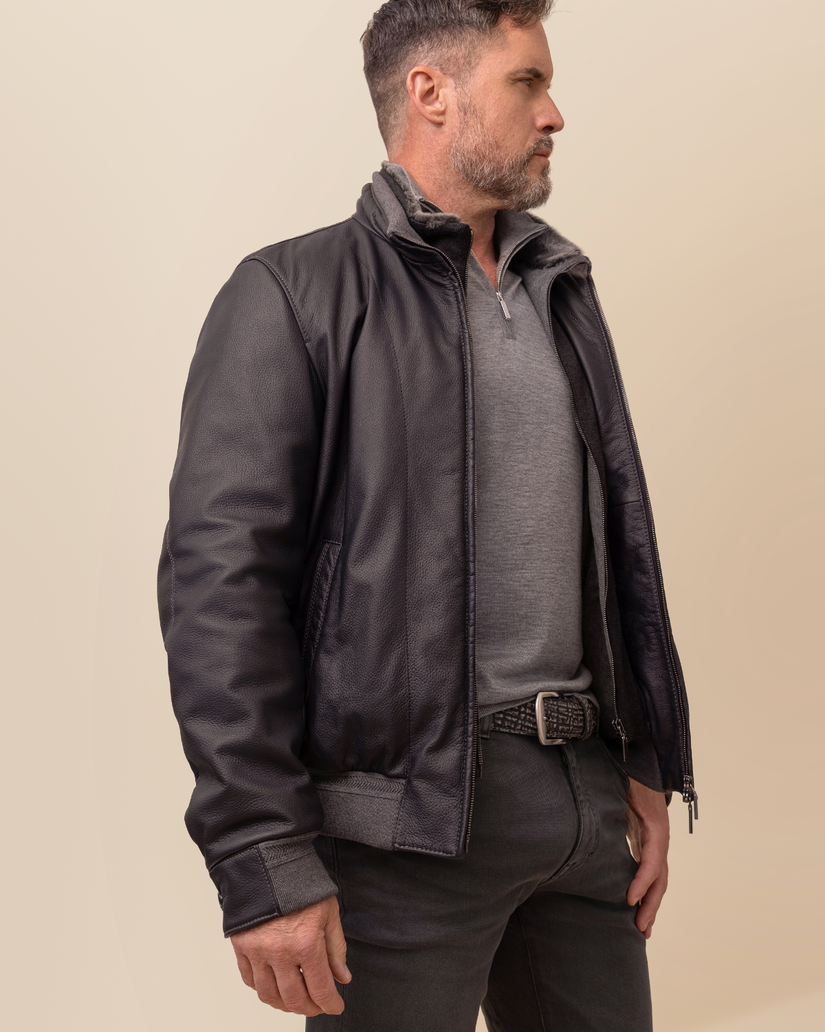 Man wearing a dark leather jacket over a gray shirt on a beige background