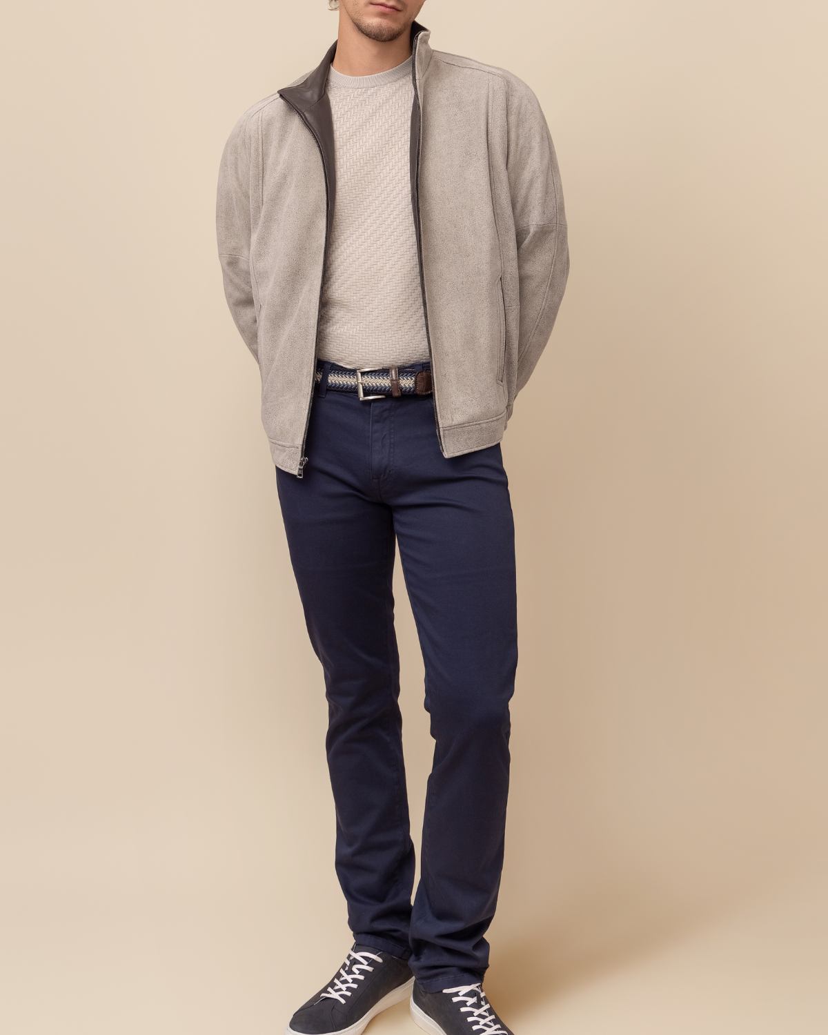 Man wearing a gray jacket, white shirt, navy pants, and black shoes on a beige background