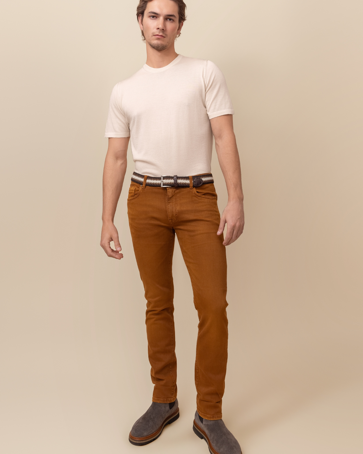 Man wearing a white t-shirt and brown pants against a beige background