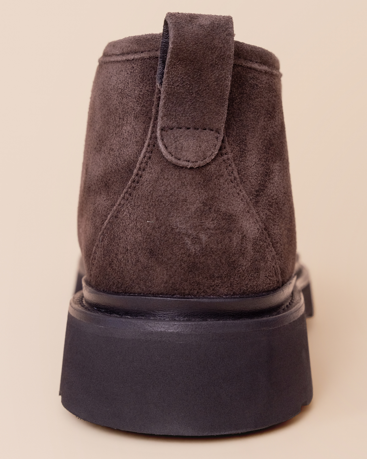 Brown suede boot with a black sole on a beige background