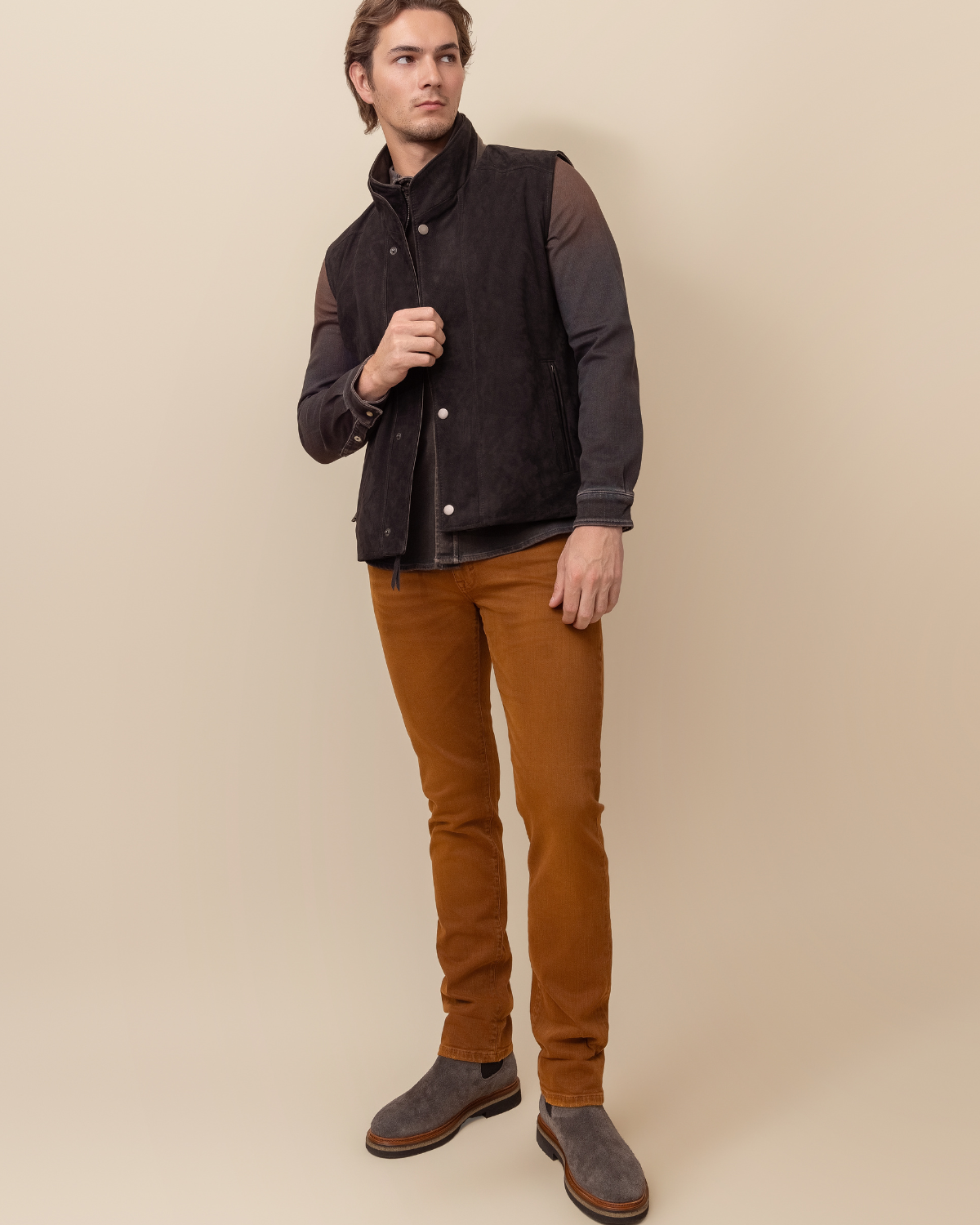 Man wearing a dark jacket and brown pants against a beige background