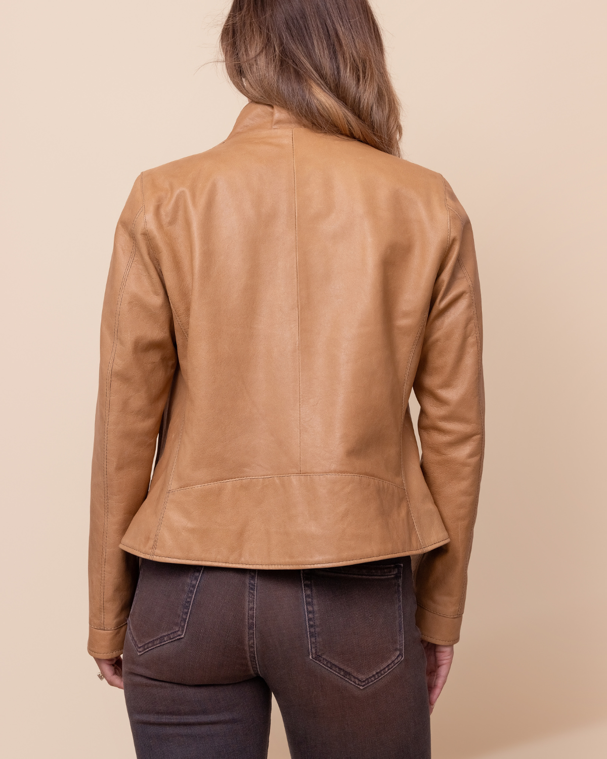 Person wearing a tan leather jacket on a beige background