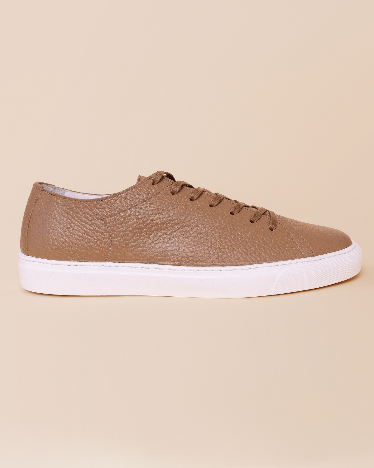 Brown leather sneaker with white sole on a beige background