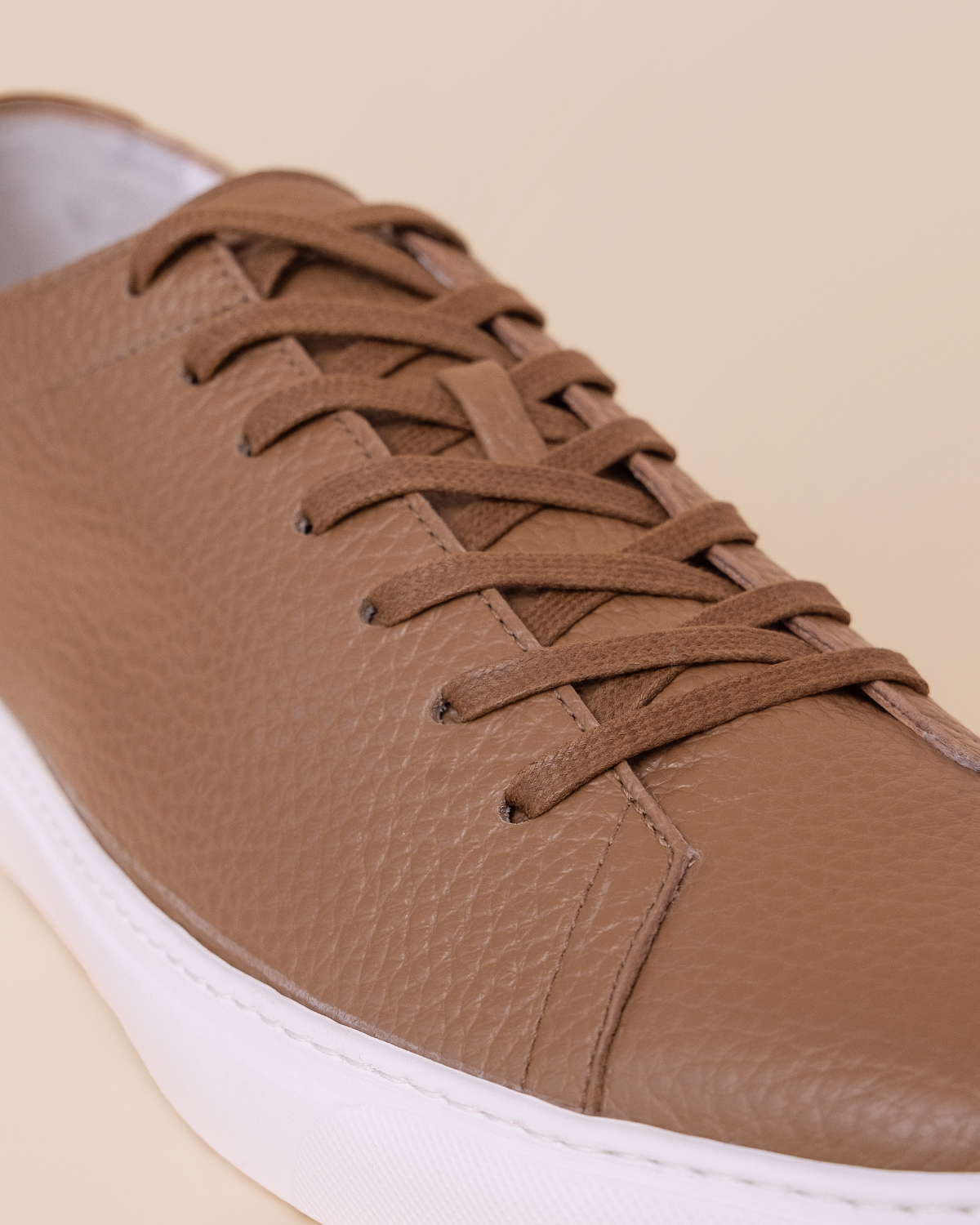 Brown leather sneaker with white sole on a beige background