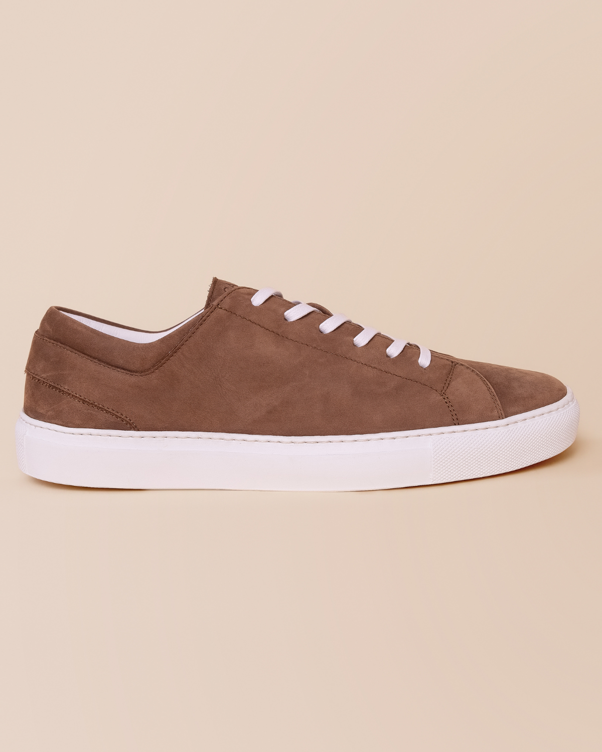 Brown sneaker with white laces on a beige background