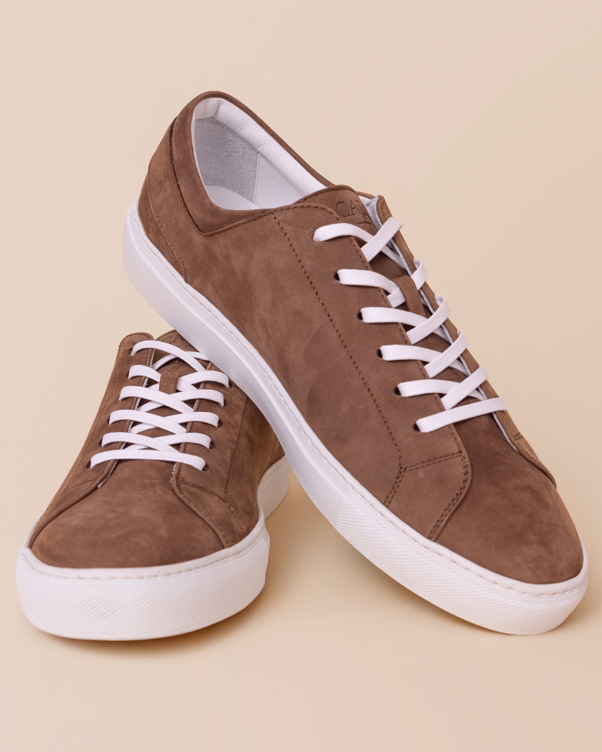 Brown nubuck suede sneakers with white laces on a beige background