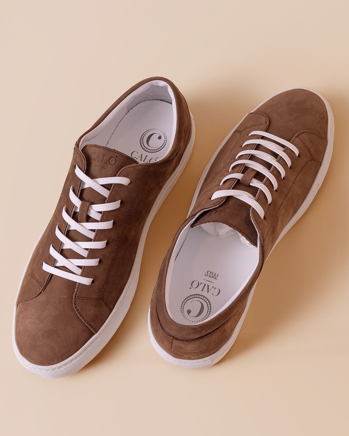 Pair of brown leather nubuck suede sneakers with white laces on a beige background