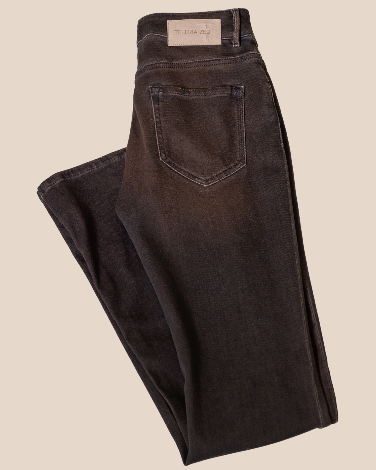 Folded black jeans with a visible brand label on a beige background