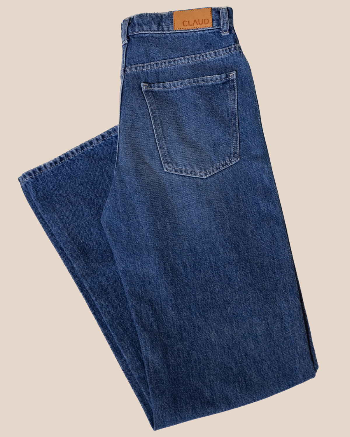 Folded blue jeans with a brand label on a beige background