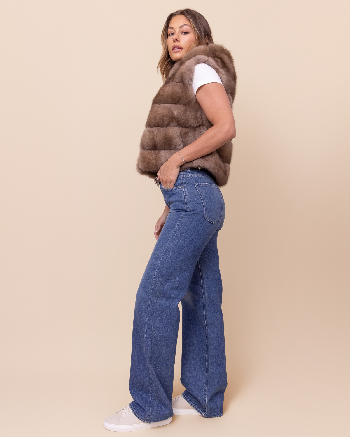Woman wearing a brown fur vest and blue jeans on a beige background