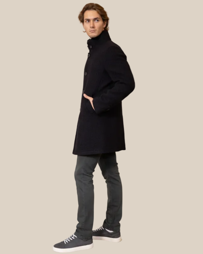 Man wearing a black coat and dark pants on a beige background
