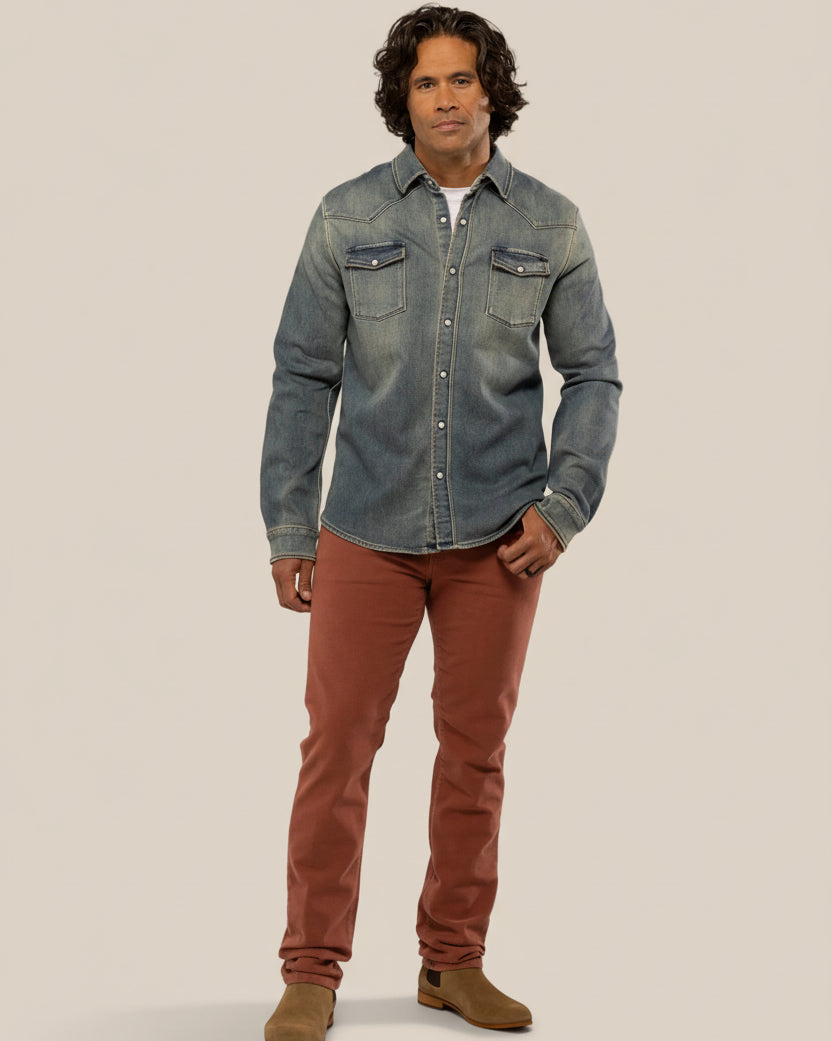 Man wearing a denim shirt and brown pants on a beige background