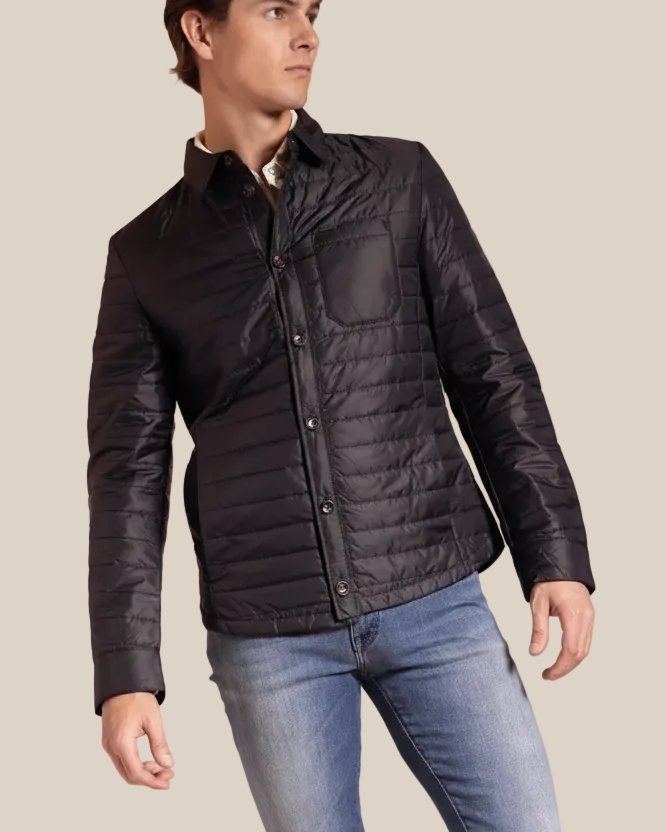 Man wearing a black quilted jacket and blue jeans on a beige background