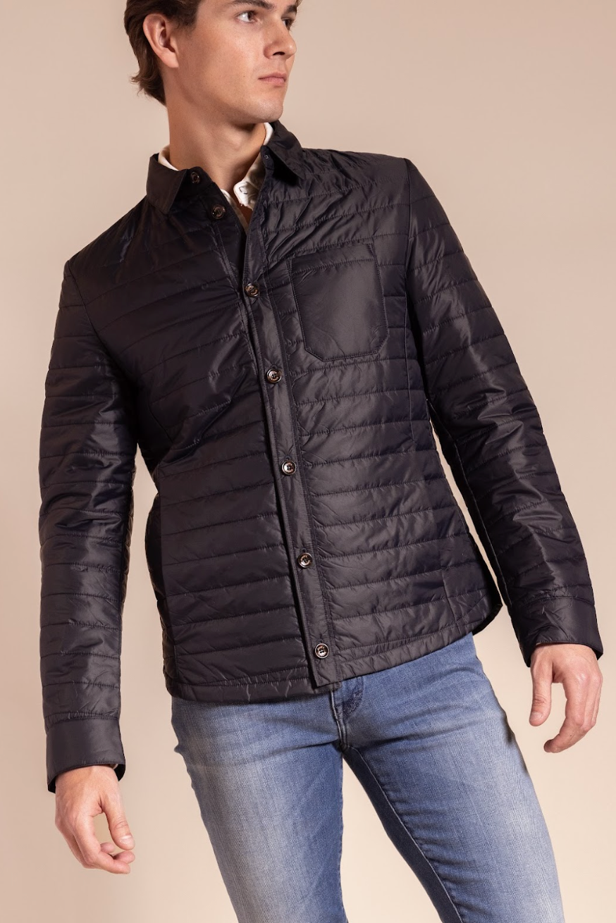 Man wearing a black quilted jacket and blue jeans on a beige background