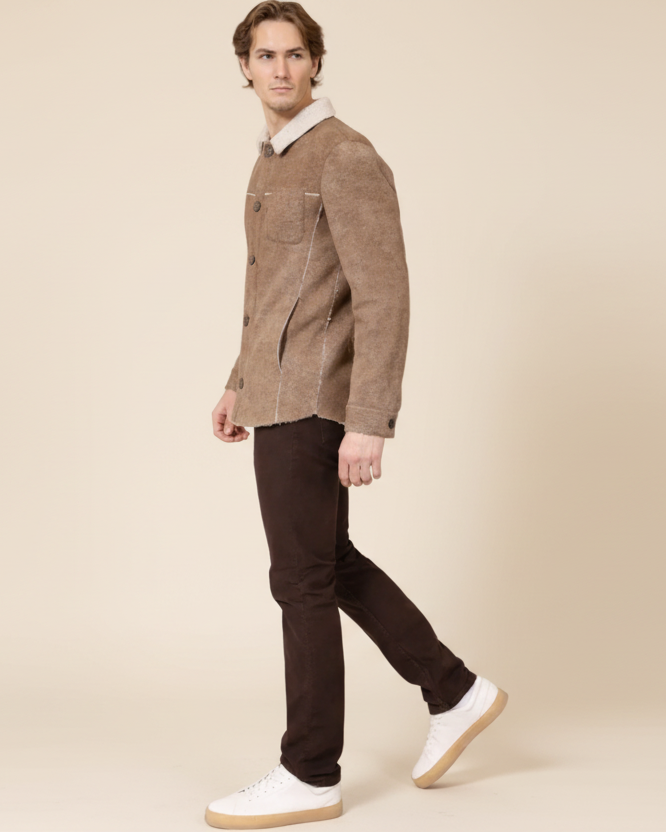 Man wearing a brown jacket with a white collar and dark pants on a beige background