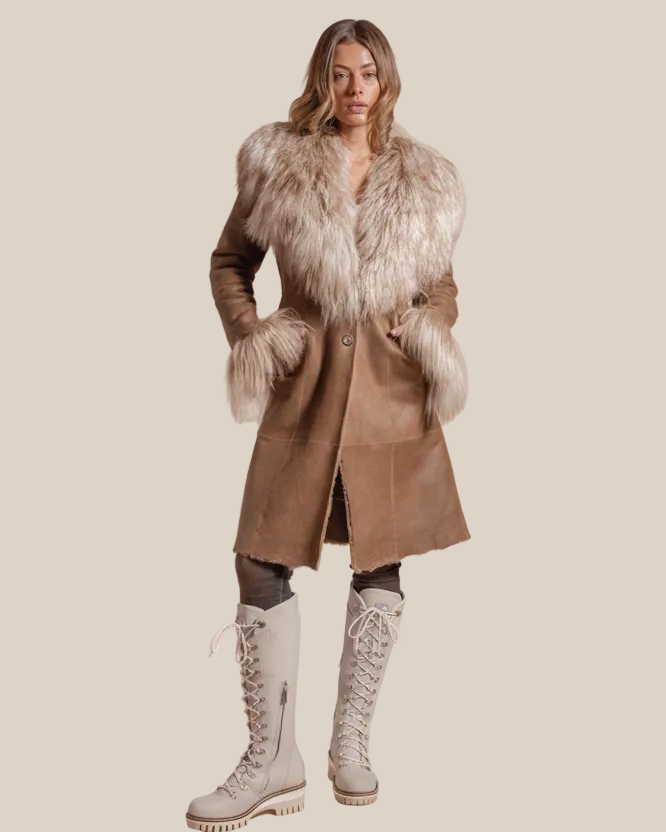 Woman wearing a long brown coat with fur trim and white boots on a beige background