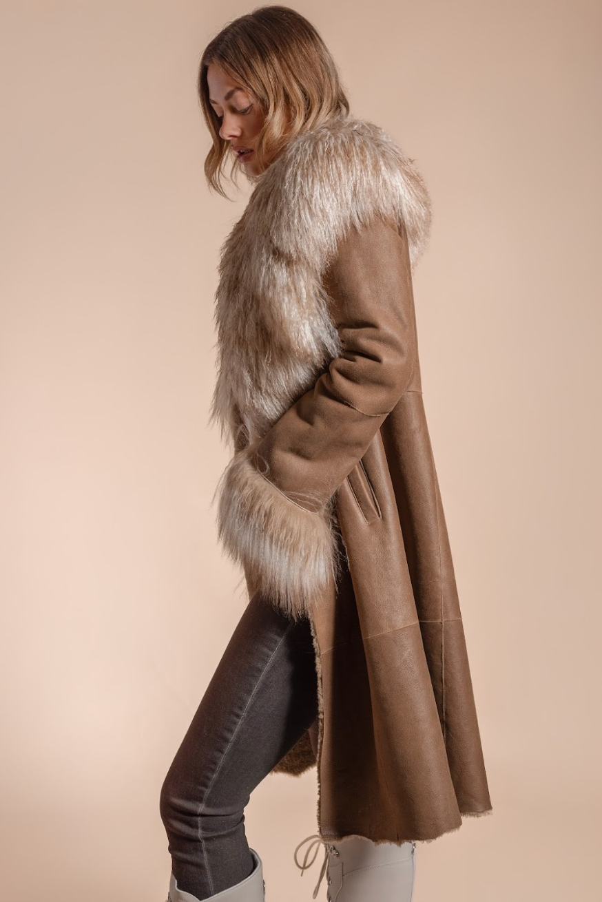 Woman wearing a long brown coat with fur trim on a beige background