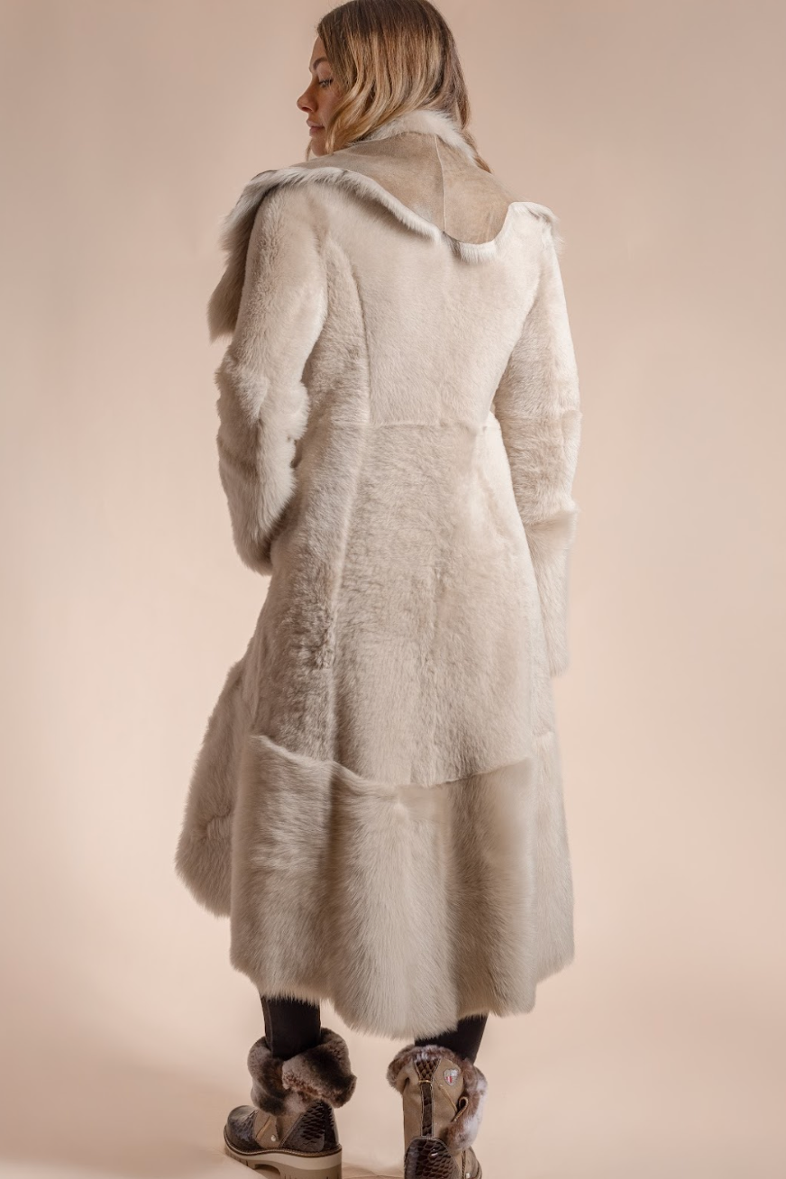 Person wearing a long, textured coat with fur trim on a plain background