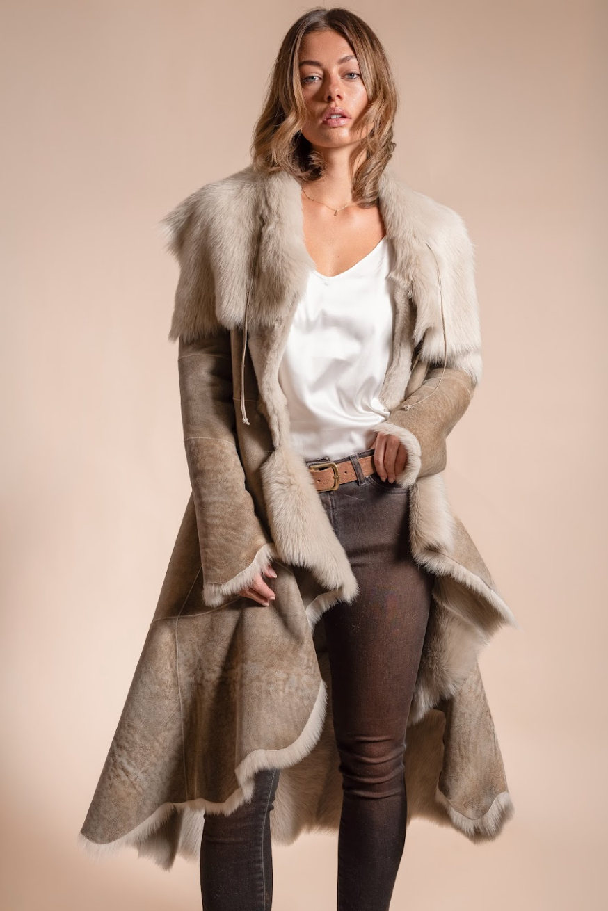 Woman wearing a long beige coat with fur trim on a beige background