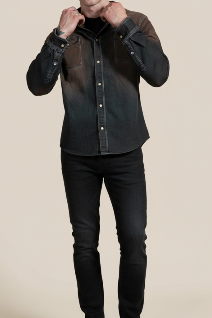Man adjusting the collar of a dark denim shirt on a beige background