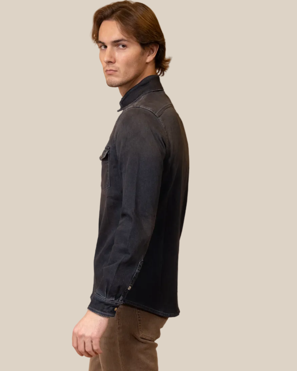 Man wearing a dark jacket and brown pants against a beige background