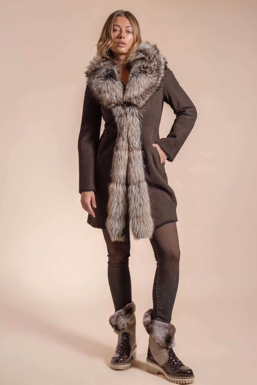 Woman wearing a long dark coat with fur trim and matching boots on a beige background