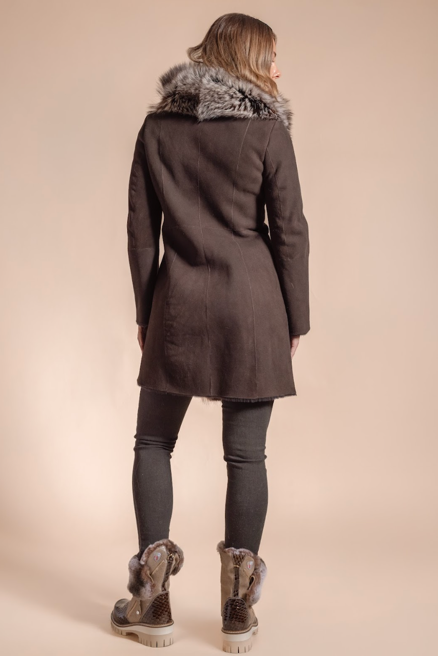 Person wearing a dark brown coat with fur trim on a beige background