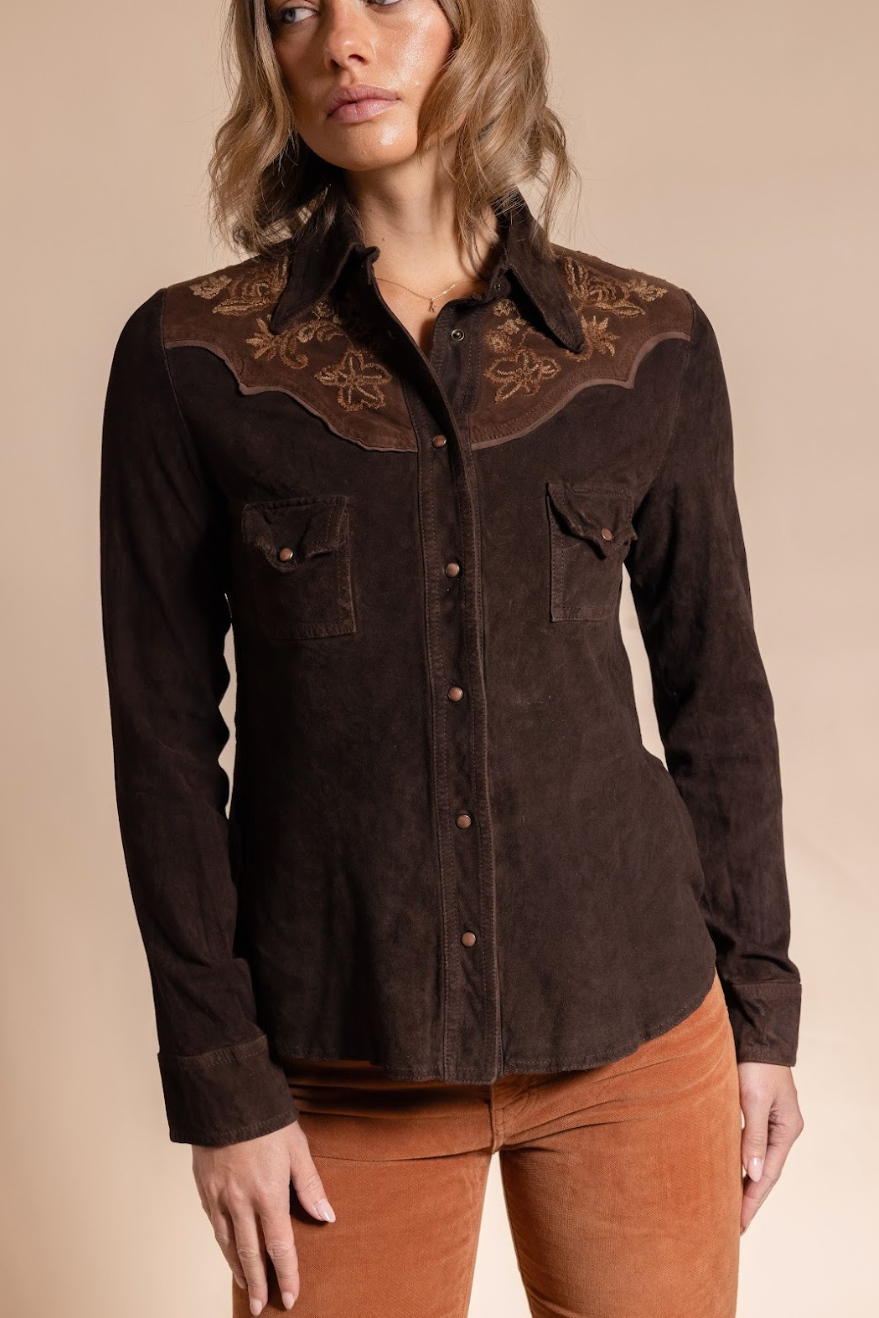 Woman wearing a brown embroidered shirt against a beige background