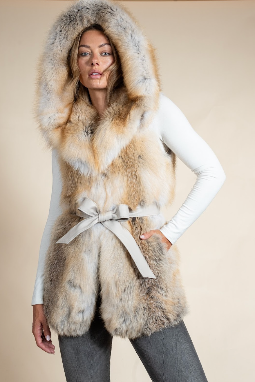 Woman wearing a fur vest with a hood on a beige background