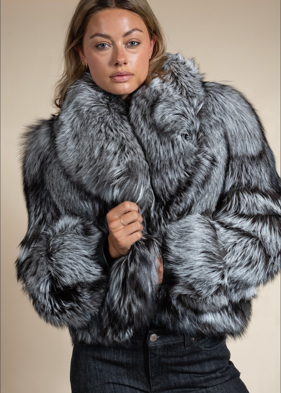 Woman wearing a gray fur coat against a beige background