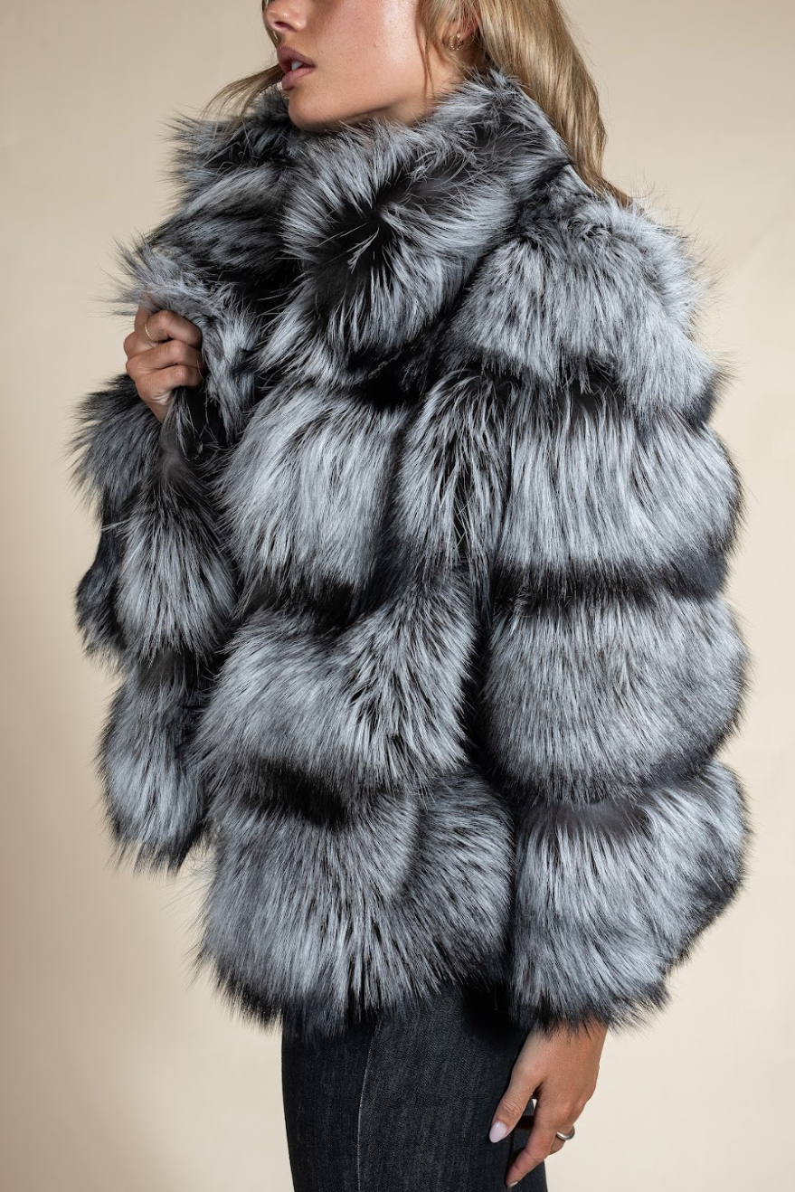 Person wearing a gray fur coat against a beige background