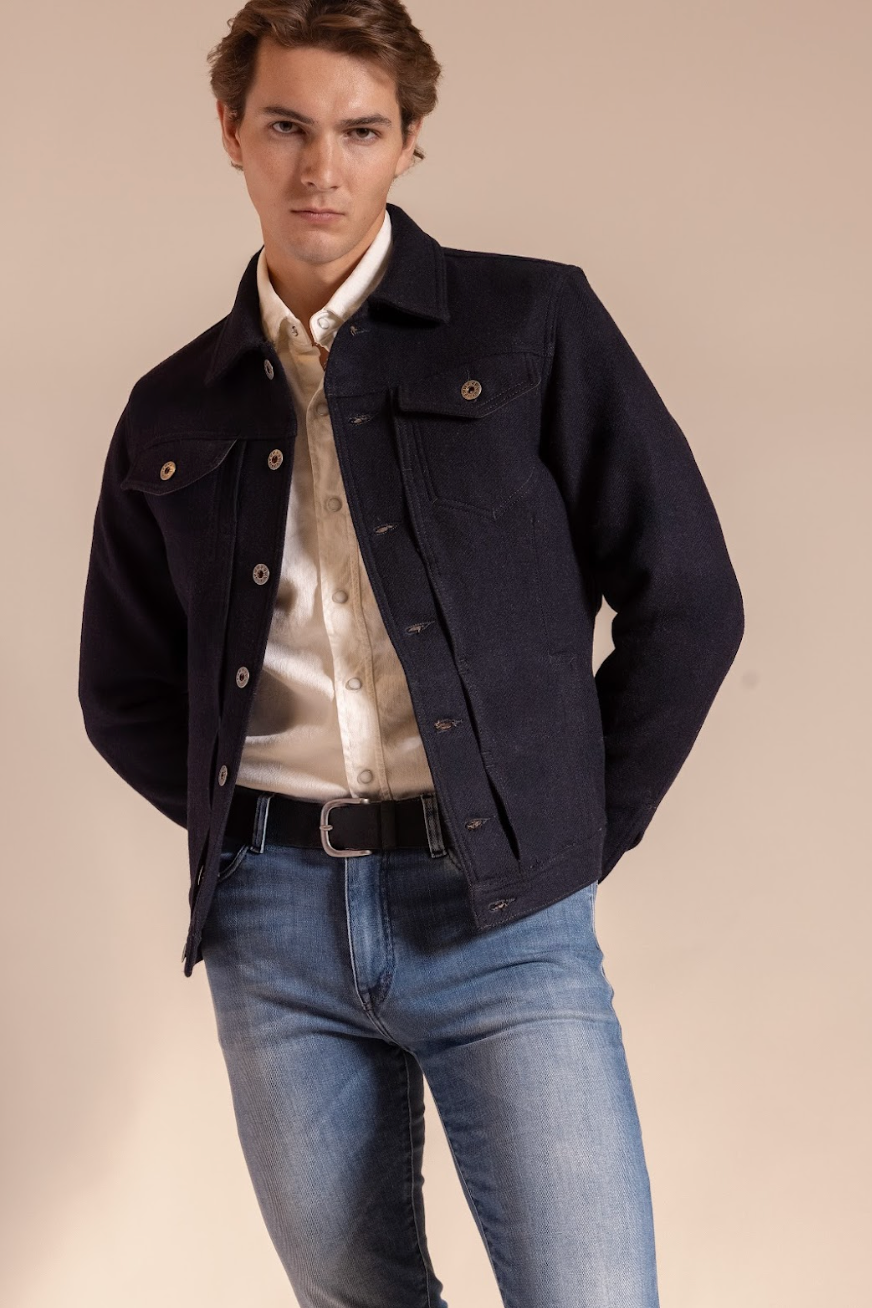 Man wearing a dark denim jacket over a light shirt and jeans on a beige background