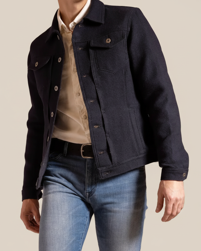 Person wearing a dark denim jacket over a light shirt and blue jeans on a beige background