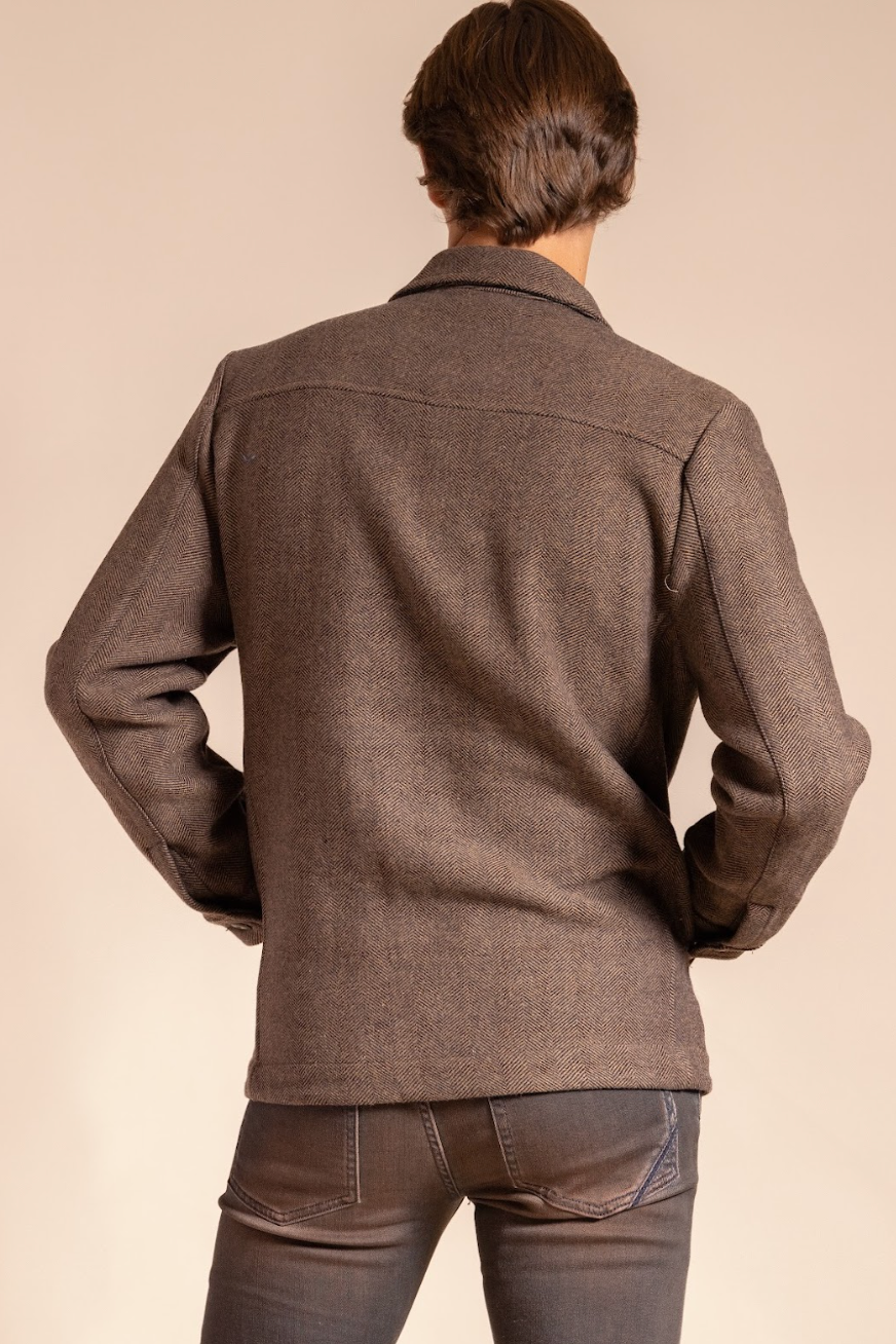 Person wearing a brown jacket and jeans on a beige background