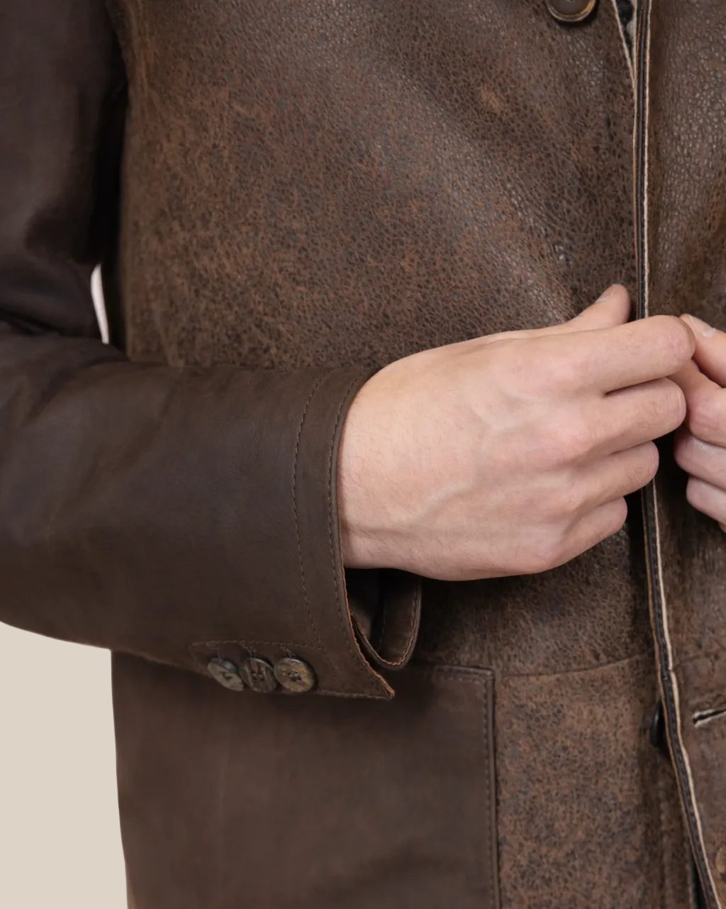 Close-up of a person adjusting a button on a brown coat against a light pink background