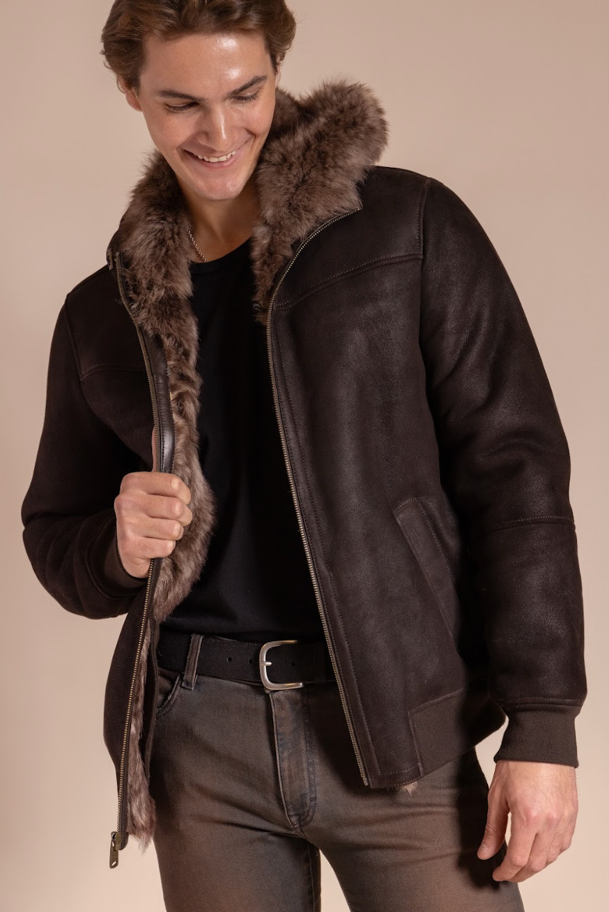 Man wearing a dark brown leather jacket with fur trim on a beige background