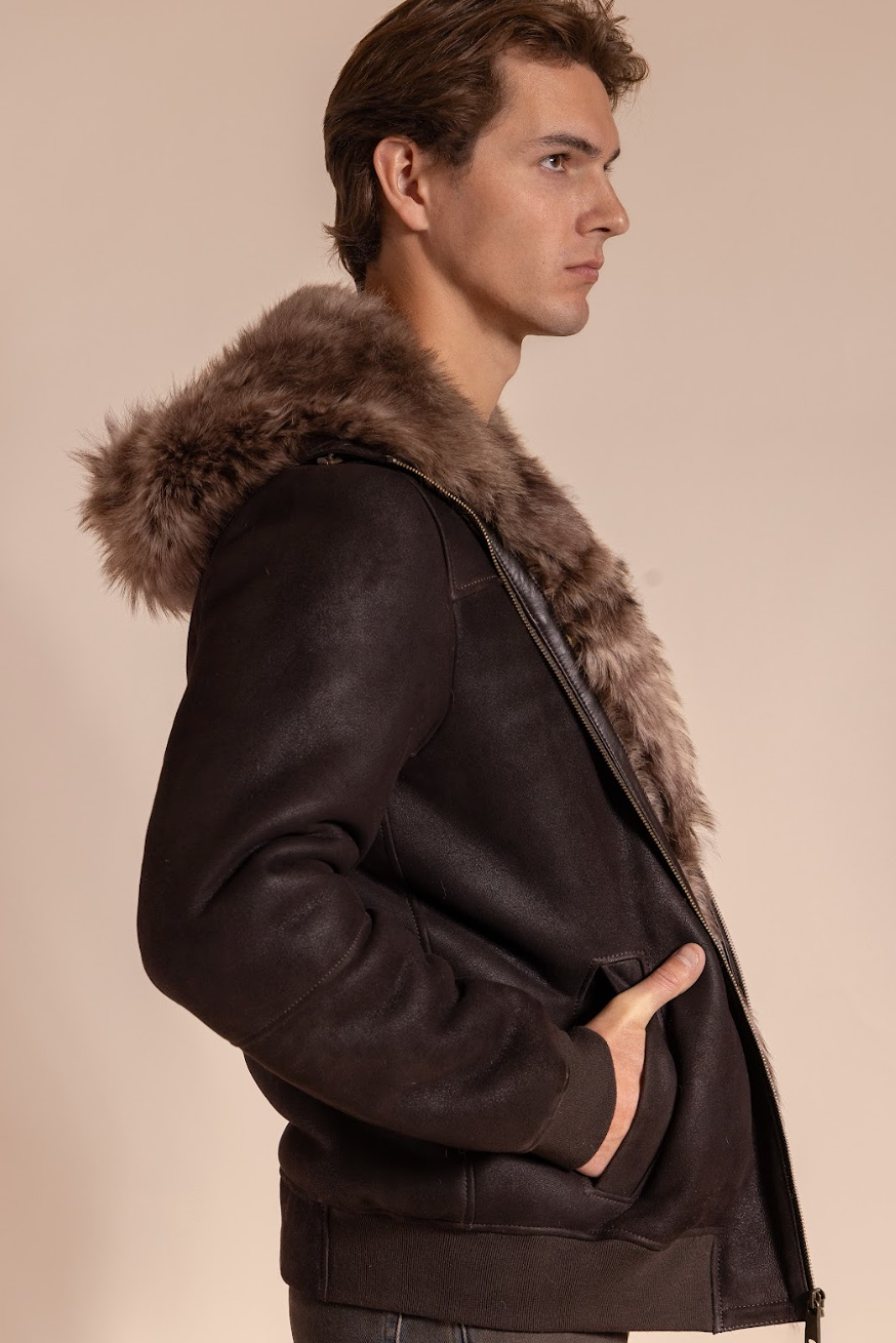 Man wearing a dark brown leather jacket with fur hood on a beige background