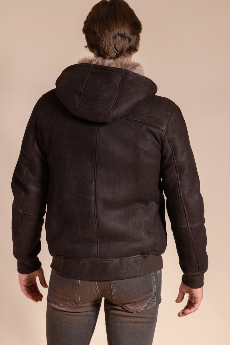 Person wearing a dark brown leather jacket with fur hood on a beige background